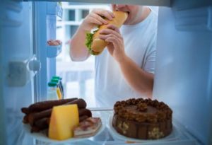 Ein Mann geht nachts an den Kühlschrank: Abnehmen bei Arthrose fällt manchmal schwer